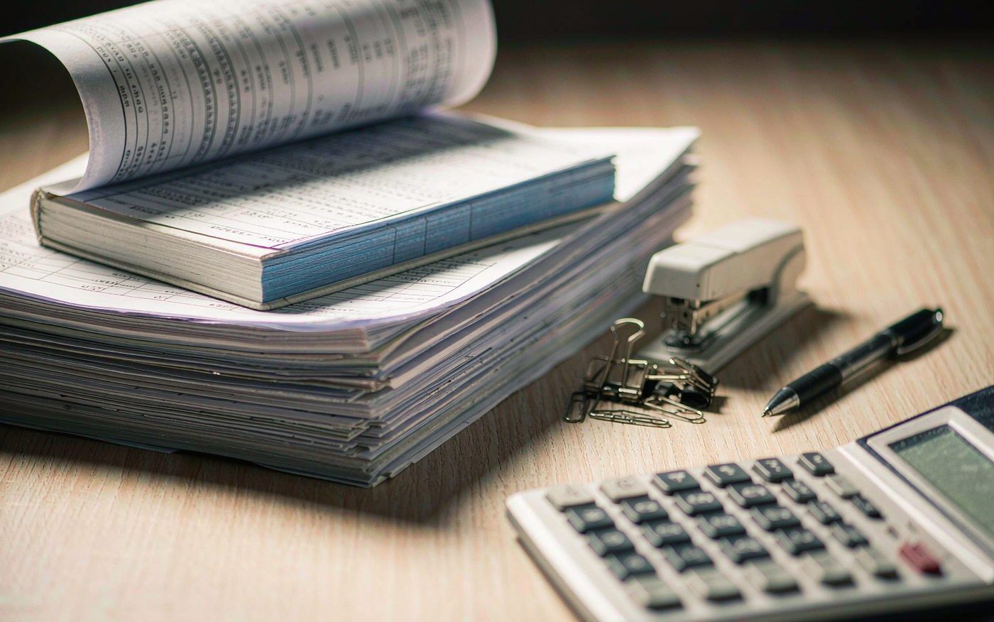 办公桌上整齐堆叠的装订凭证册、计算器与文具
