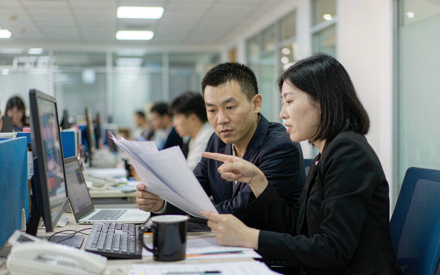 办公人员坐在工位前，对照屏幕与打印材料核对